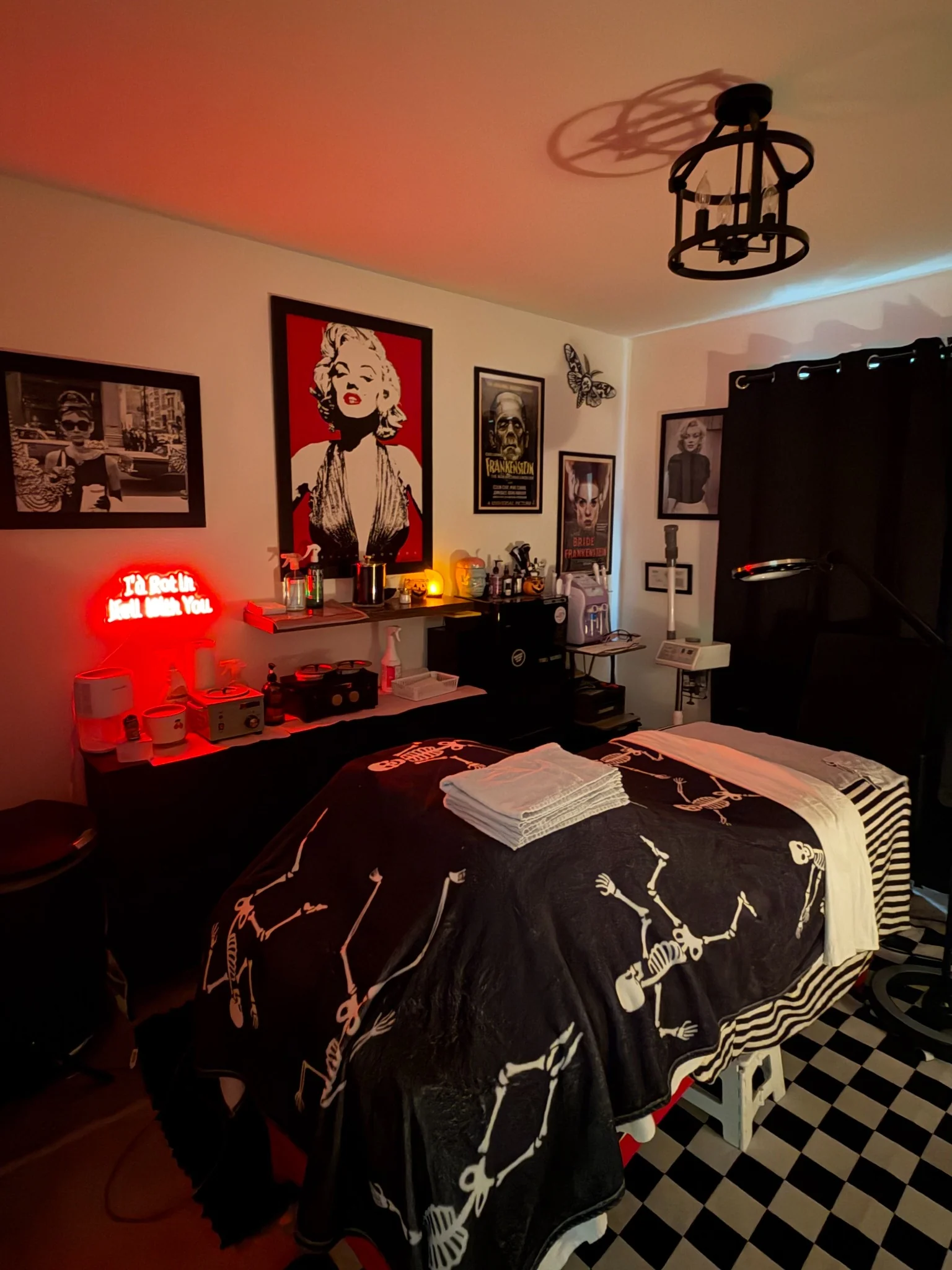 Mythical Skincare Co. treatment room with checkerboard floor, horror artwork, red lighting, and treatment table